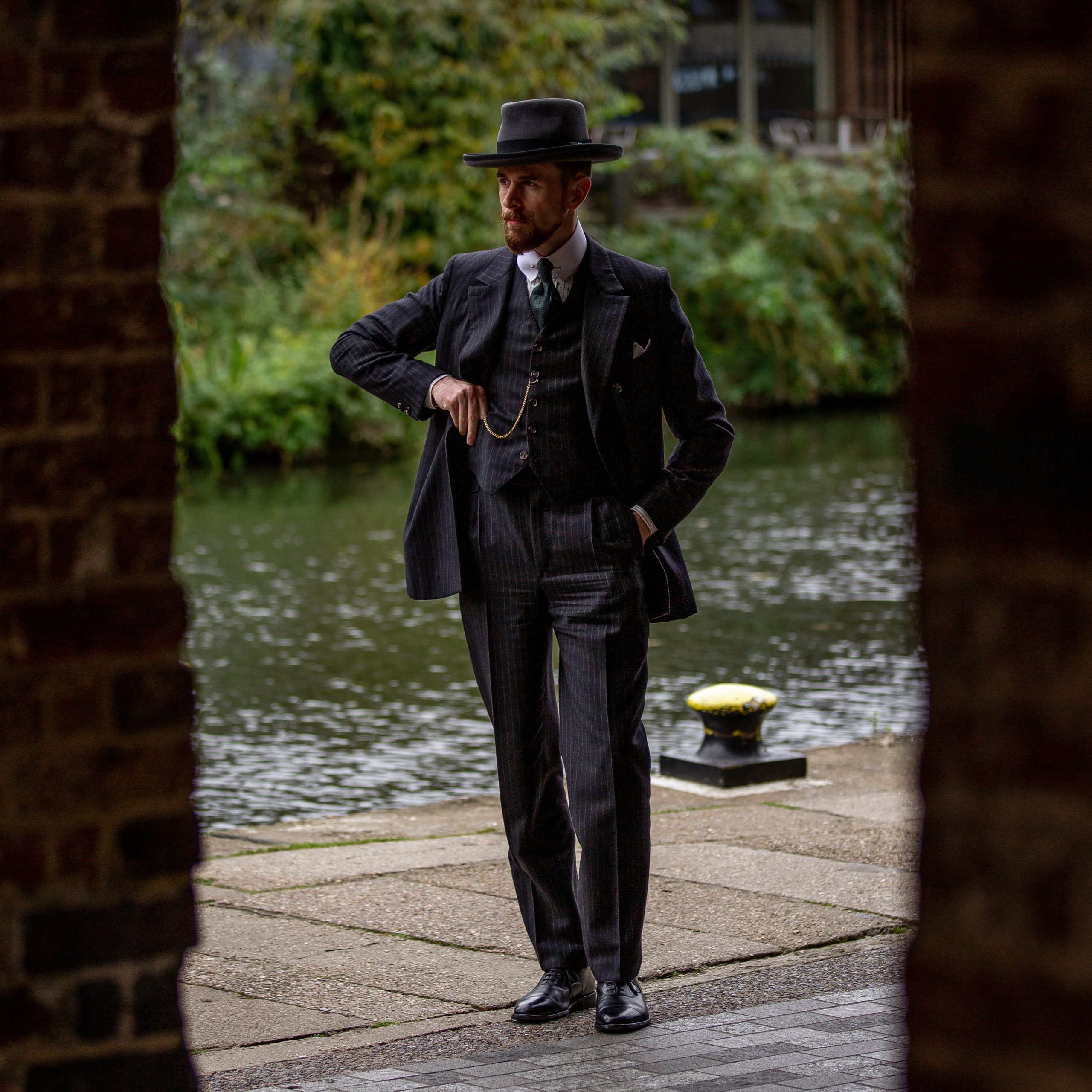 Großer, grauer Homburg (Hut), Hemd mit hohem Kragen und Dreiteiler aus schwarzem Flanell mit Kreidestreifen